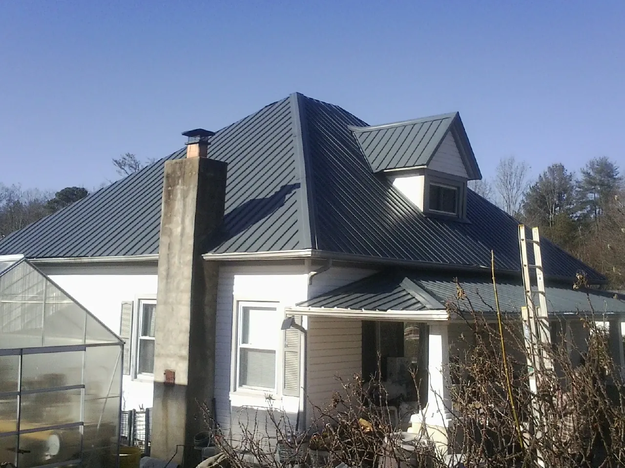 Dark blue standing seam metal roof on a white farmhouse with dormer — Slate & Tile Roof Repair by Roofing Brothers in Metamora