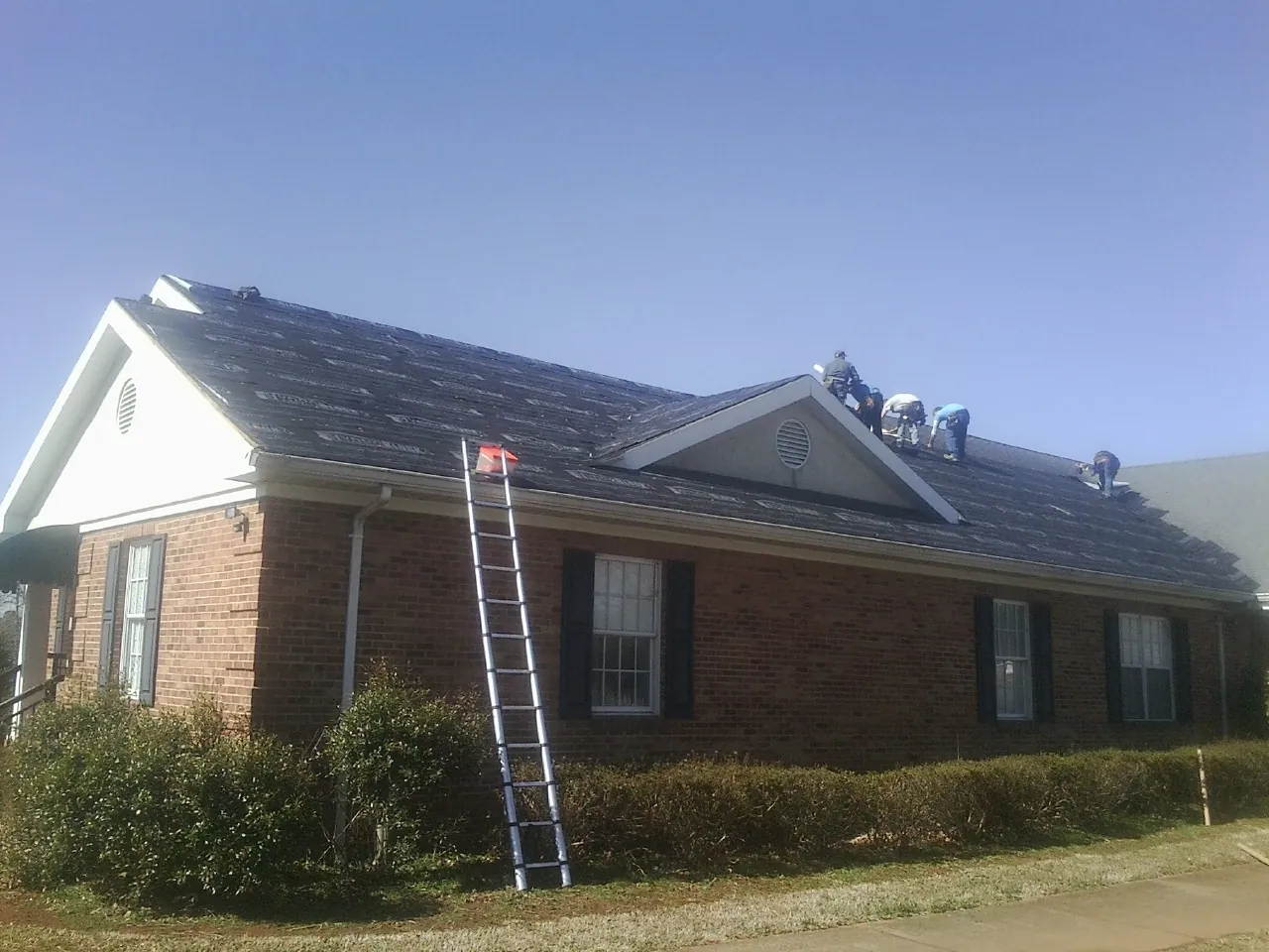 Crew tearing shingles off a brick ranch roof with a ladder set — Emergency Roof Repair work by our crew in Metamora